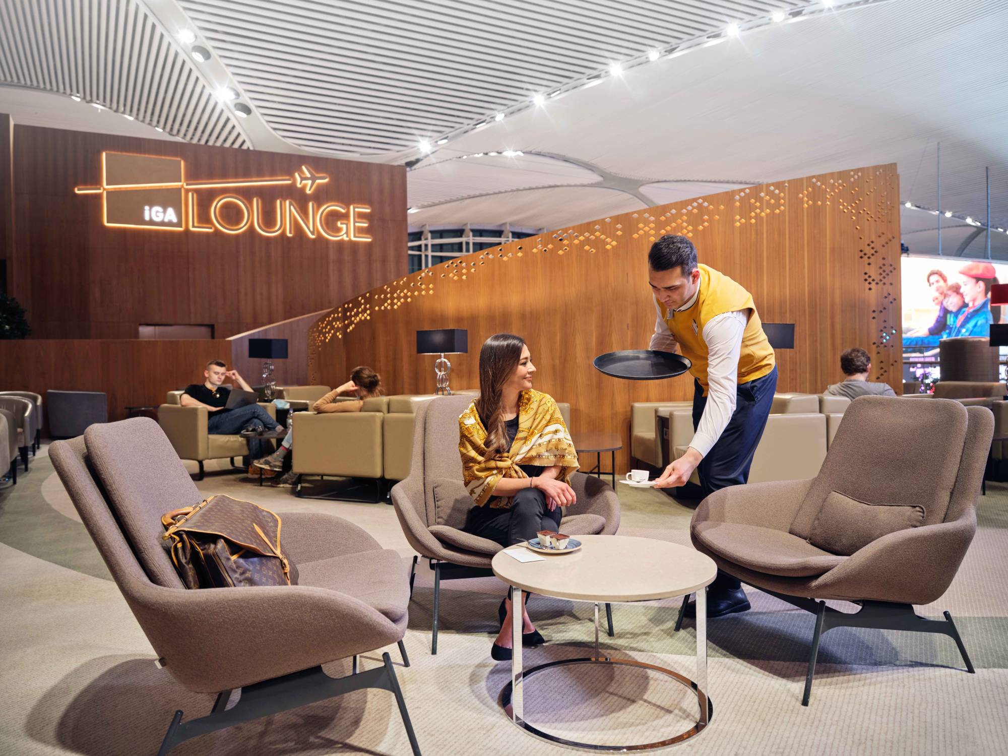 a passenger sitting at iga lounge and a waiter serving cofee